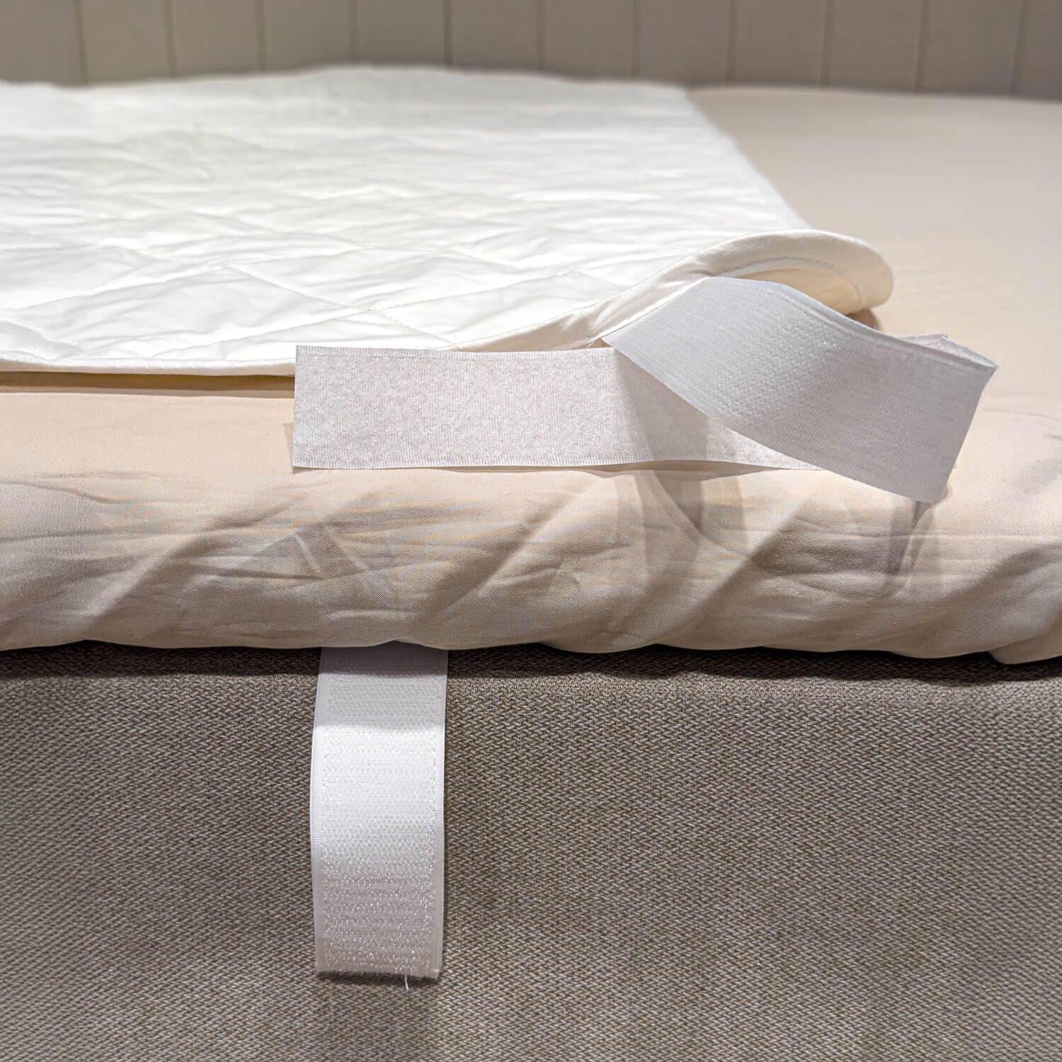 Η γωνία του λευκού καπιτονέ προστατευτικού στρώματος διπλωμένη προς τα πίσω, ώστε να φαίνεται ο ιμάντας βέλκρο γύρω από την άκρη του κρεβατιού